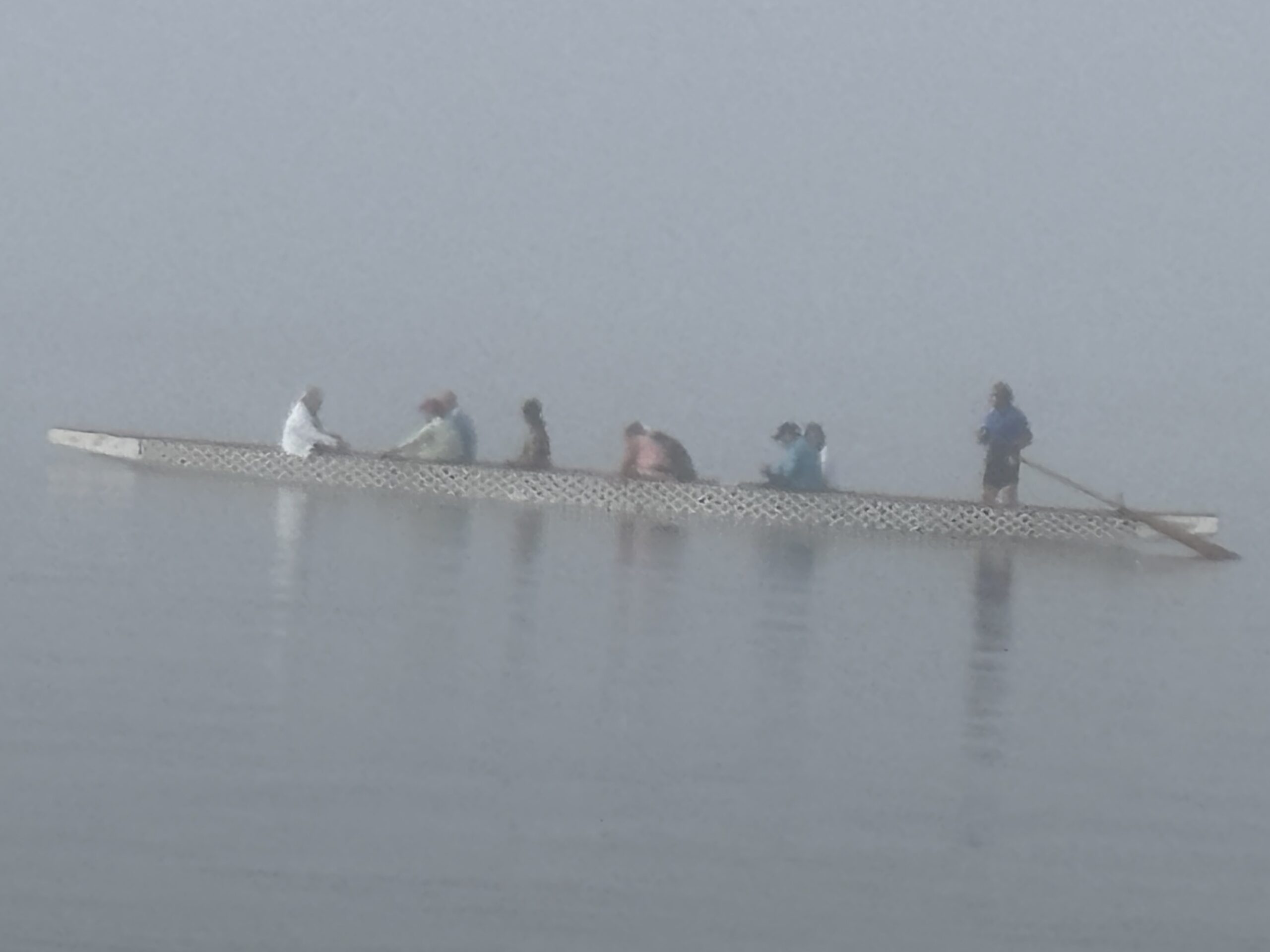 A rowing team moving together across calm water in the mist
